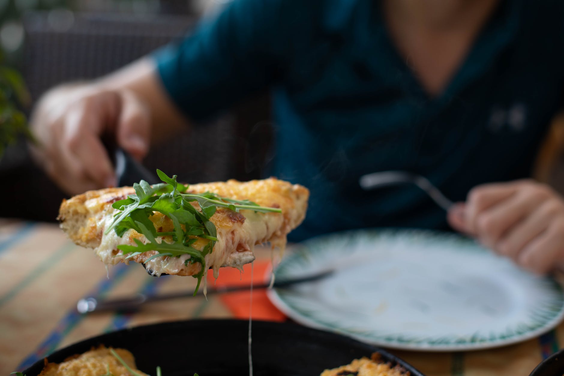 faceless man showing appetizing pizza with arugula in restaurant